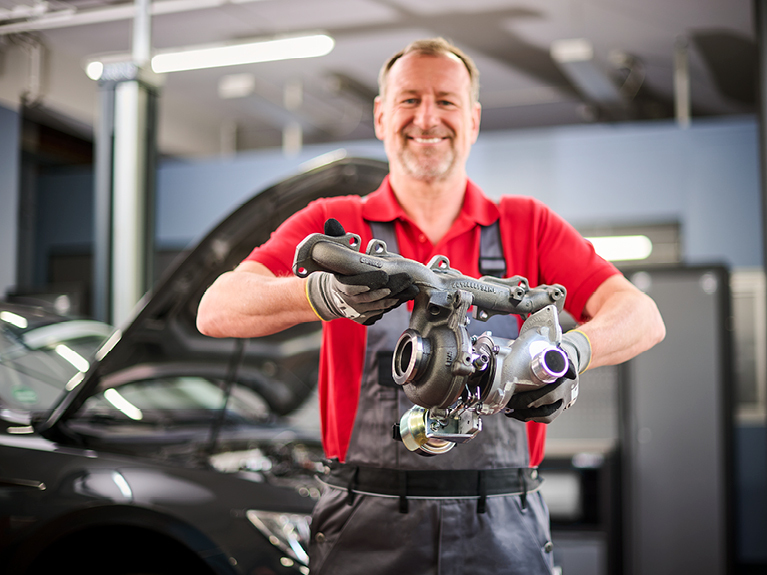 mechanic in a workshop environment, proudly holding turbocharger components